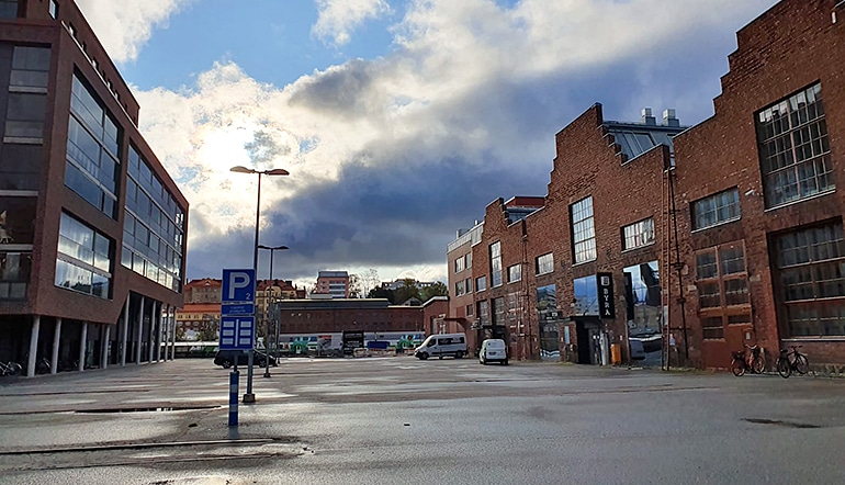 P-Logomo P2 Turku, näkymä punatiilisten rakennusten ympäröimälle asfaltoidulle parkkialueelle P2 kadulta katsottuna