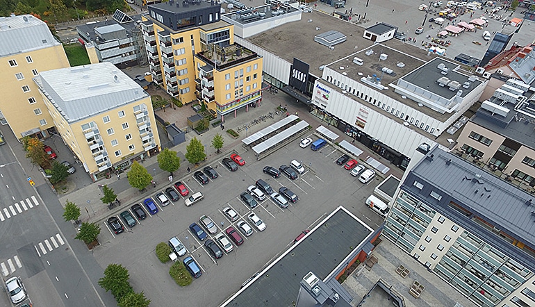 P-Sokos Kuopio, ilmakuvassa kaupungin rakennuksia, katuja, autoja parkkipaikalla ja taustalla tori