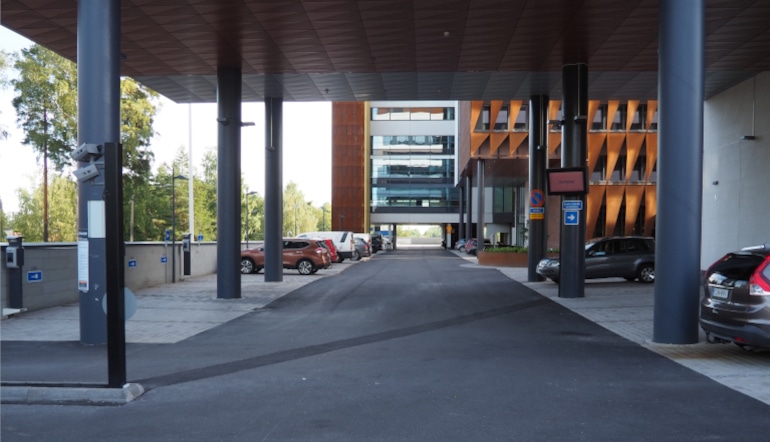 P-Swing House Espoo, katettu parkkipaikka ja taustalla toimistorakennus sekä puita