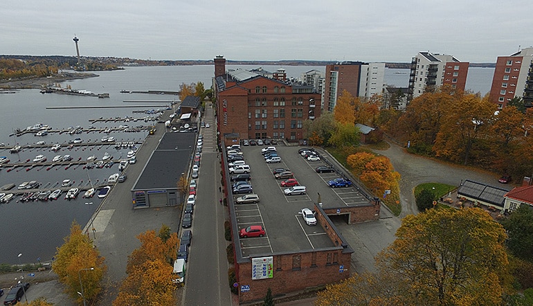 P-Tampereen kylpylä Tampere, ilmakuvassa parkkipaikka punatiilisen rakennuksen katolla meren rannan läheisyydessä
