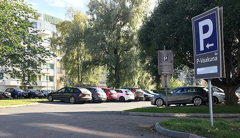 P-Vaakuna Hämeenlinna, autoja puiden ja kerrostalorakennusten ympäröimälla pysäköintialueella