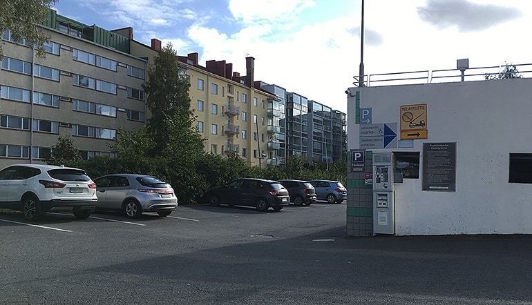 P-Vaakuna Hämeenlinna, näkymä pysäköintialueelle jonka takana on pensasaita ja sen takana kerrostaloja