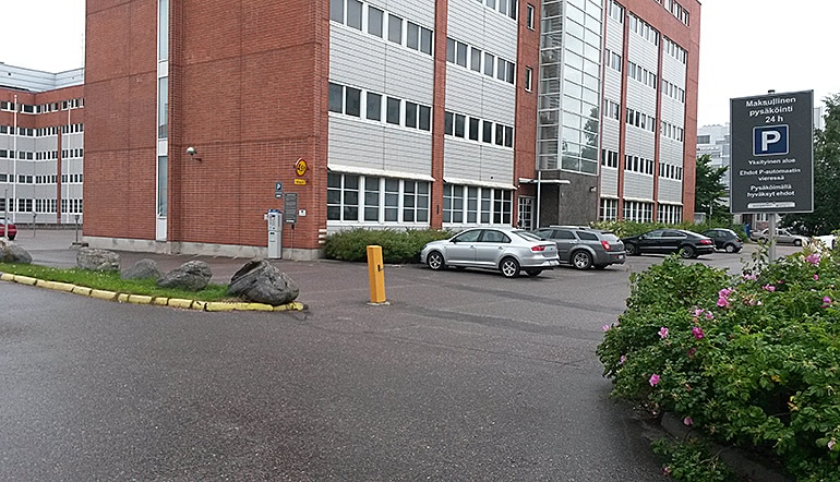 P-Valimotie 10 Helsinki, asfaltoitu pysäköintialue toimistorakennuksen edessä kadulta katsottuna