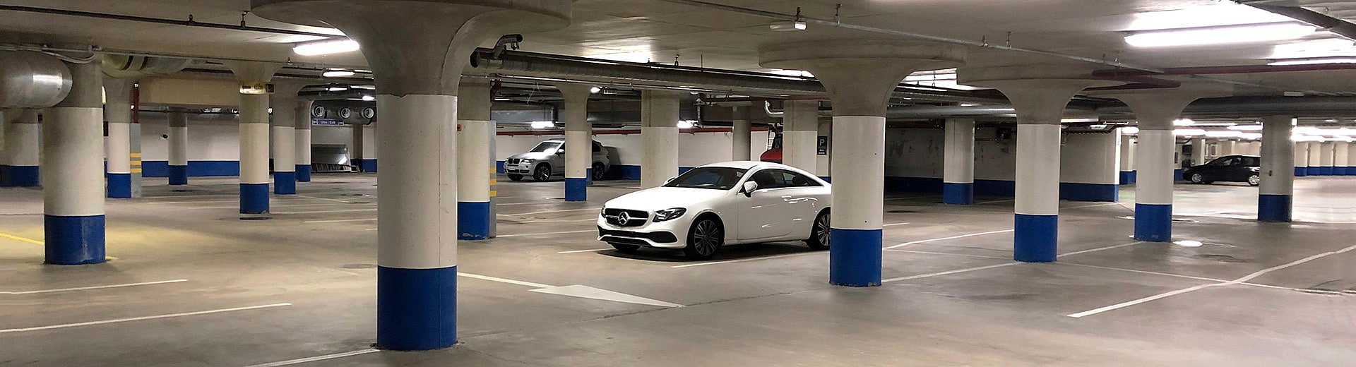 Valokuva parkkihallista, jossa on pysäköitynä muutama auto, lähimpänä valkoinen Mercedes-Benz.