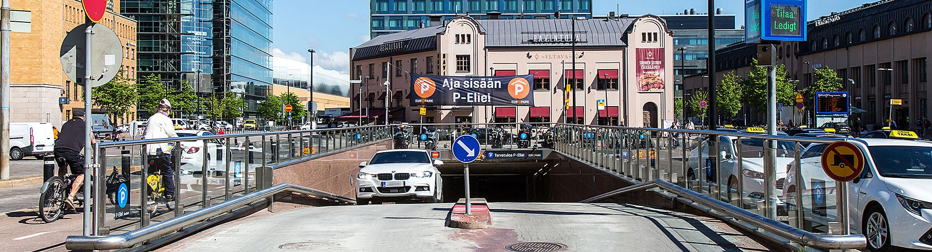 Elielin hallin sisäänajo, josta valkoinen auto on poistumassa.